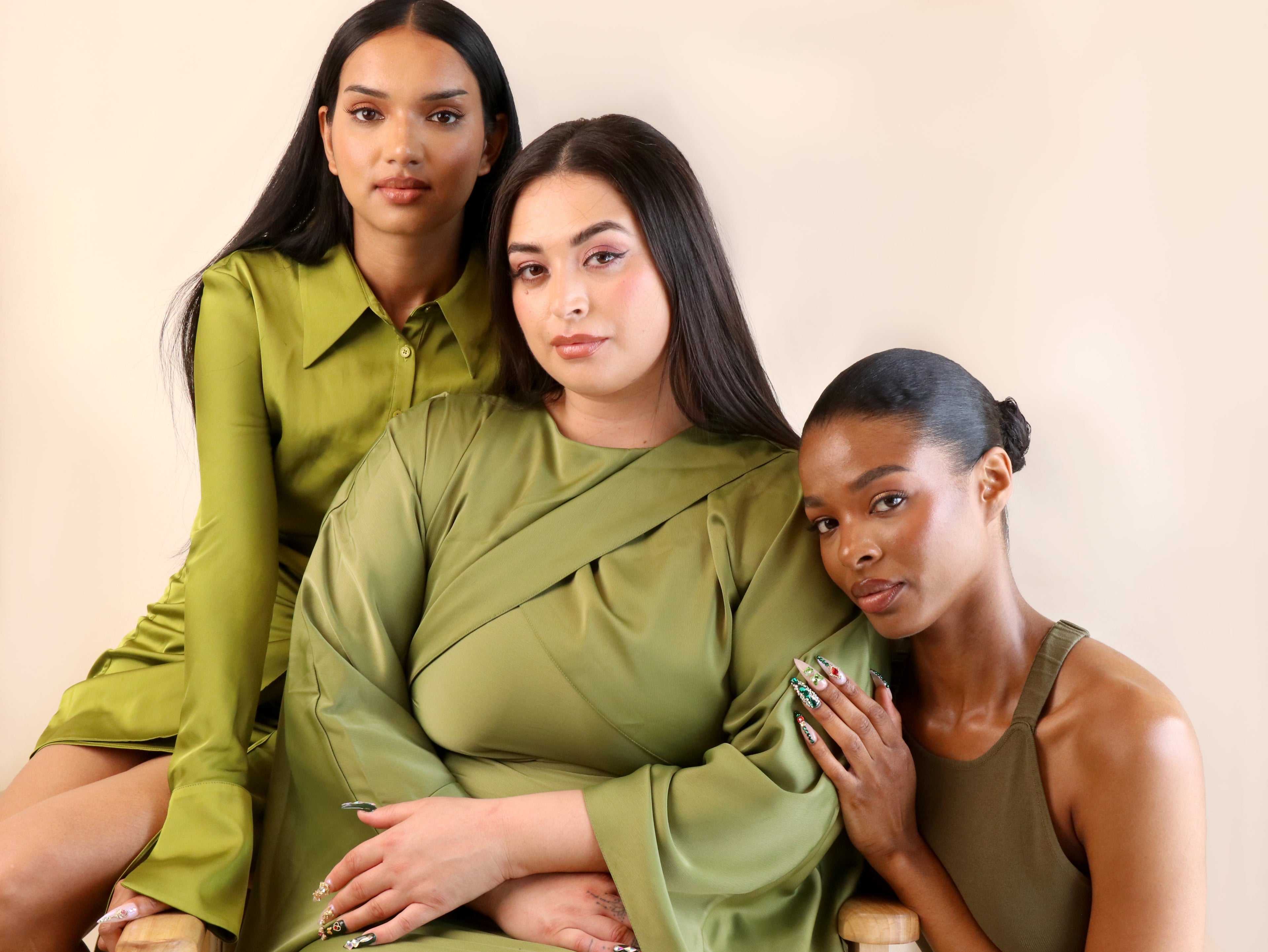 Three women wearing green outfits against a beige background