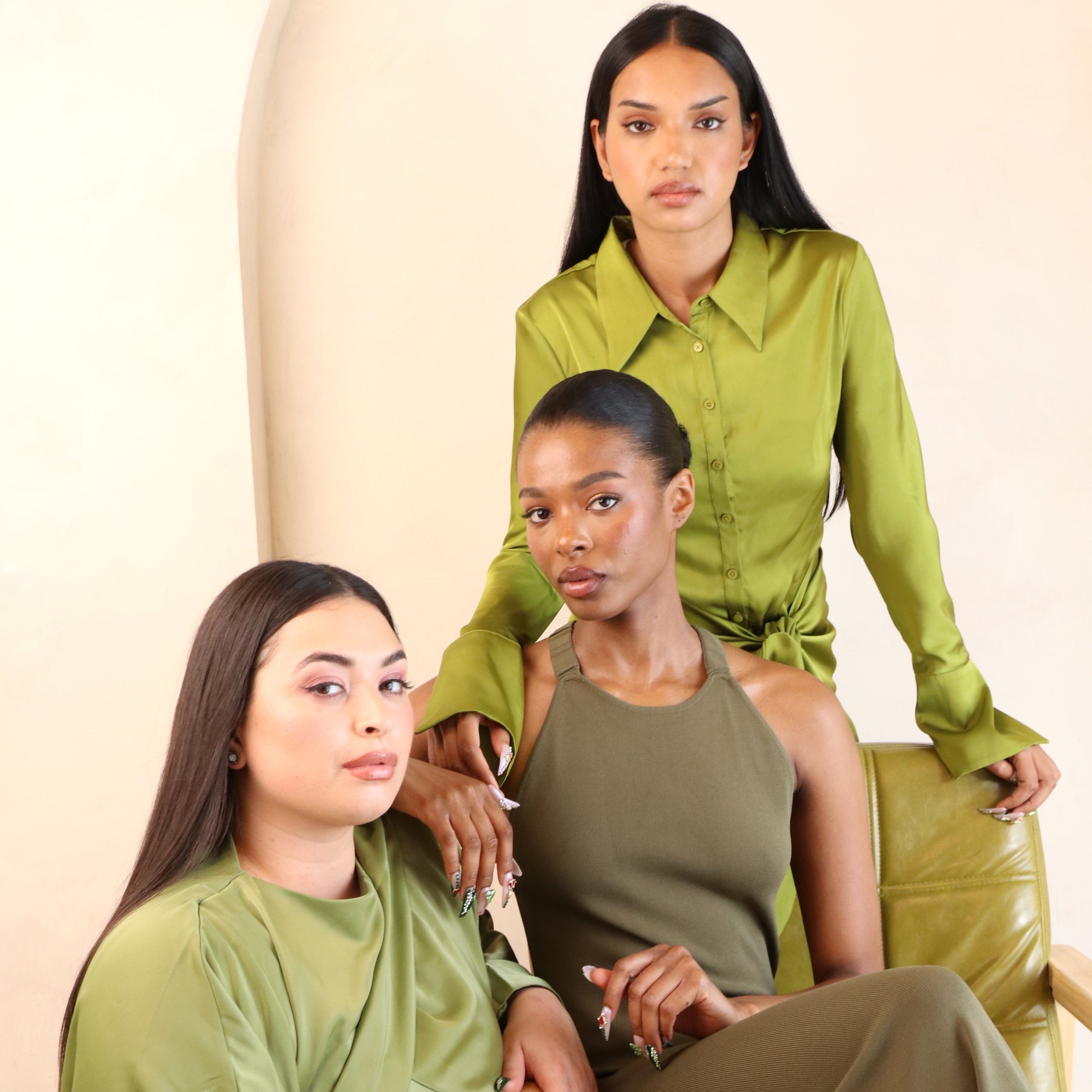 Three people in green outfits posing together on a beige couch.