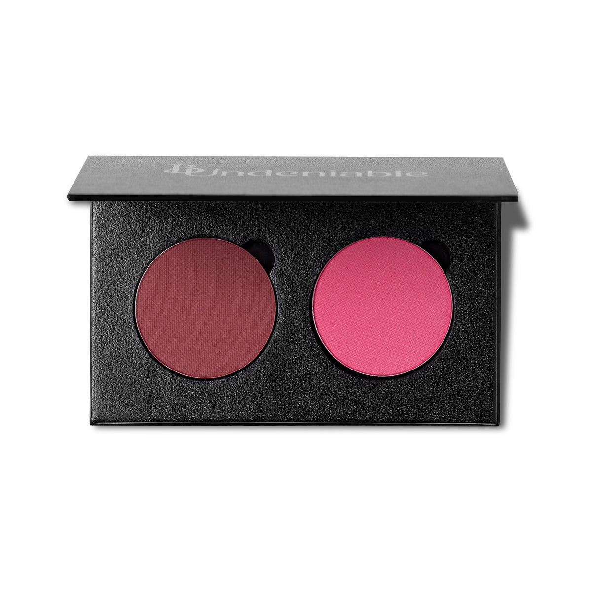 An open black makeup palette with two round pressed powder pans, one muted berry red and one bright pink, on a white background. The brand name 'B:Undeniable' is printed in white on the lid.