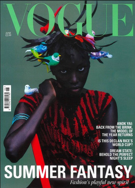 Vogue magazine cover with a model wearing a colorful headpiece and red outfit against a green background.