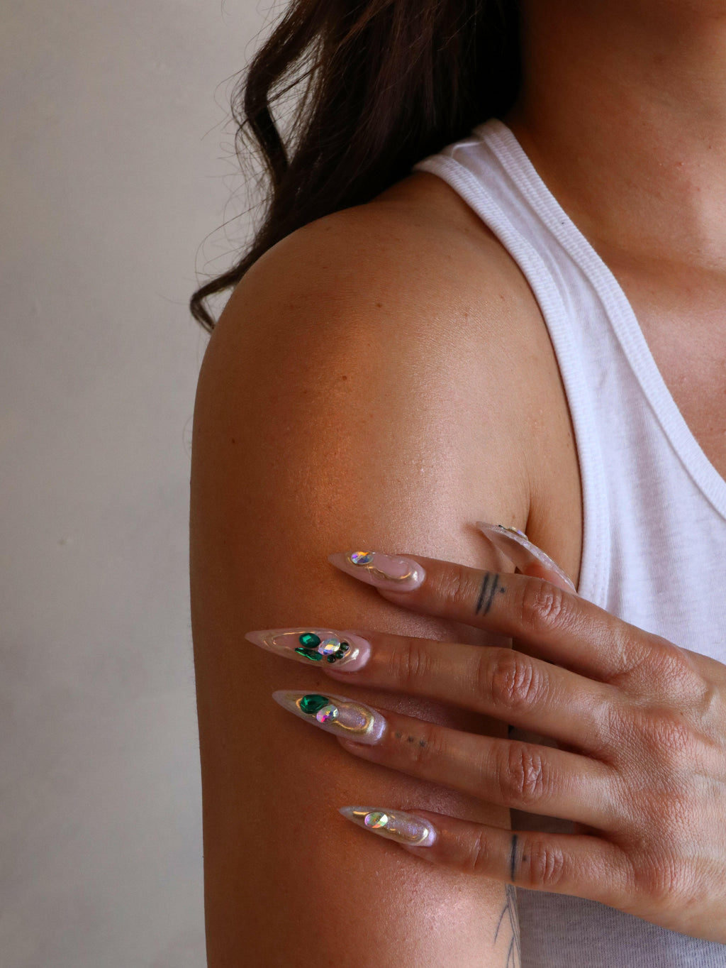 Close-up of a person's arm with long, decorated nails against a neutral background